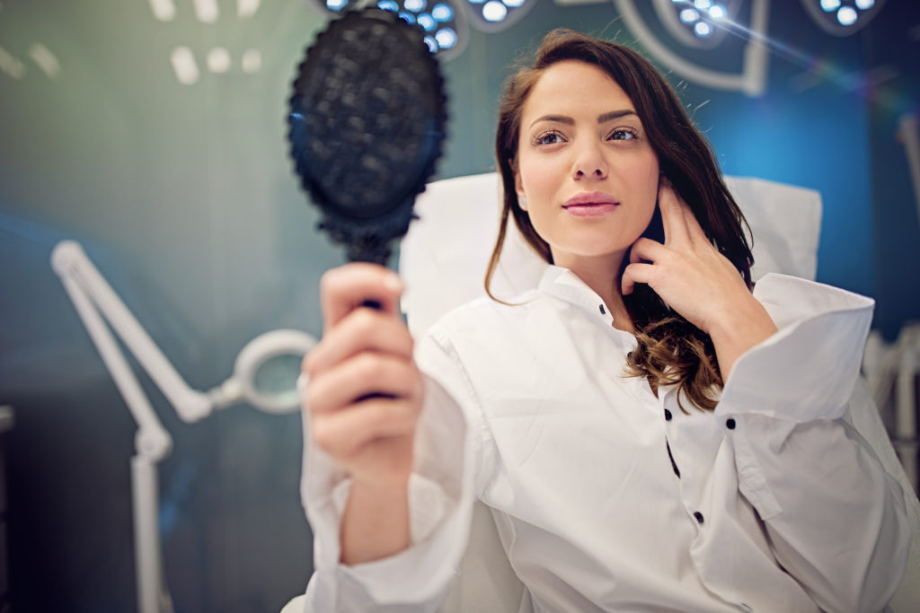 Young woman is looking her face in the mirror after lip enhancement procedure.