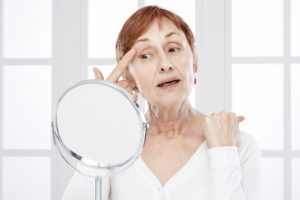 Mature woman with finger on skin looking to the mirror.