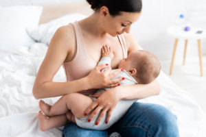 caring mother breastfeeding baby boy in bedroom