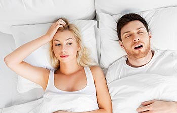 unhappy woman lying in bed with snoring man
