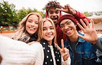 Group if cheerful multiethnic friends teenagers spending fun time together outdoors, taking a selfie