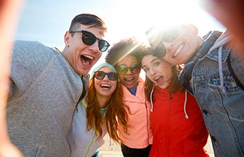 group of happy laughing teenage friends taking selfie outdoors