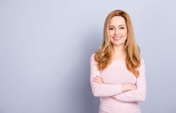 Woman showing white teeth in her smile standing with her arms folded.