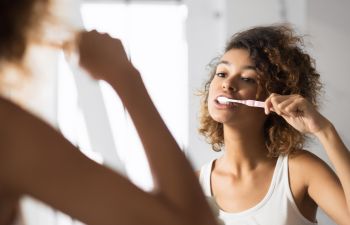 Afro-American woman looking at herself in the mirror while brushing teeth.
