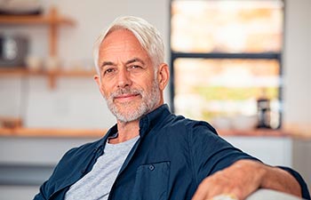 Handsome senior man with white hair sitting on couch and looking at camera