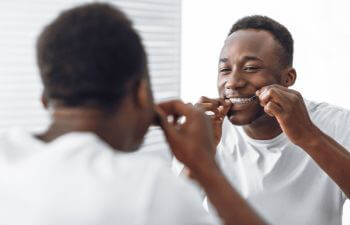 Afro-American man flossing his teeth in front of the mirror.